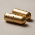 Macro photograph of two Kridavati capsules - opaque metallic gold two-piece hard shells with a visible seam.