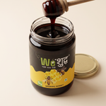 Open jar of WeShuddhs Sarang Honey with a wooden dipper lifting a thick strand of near-black raw honey.